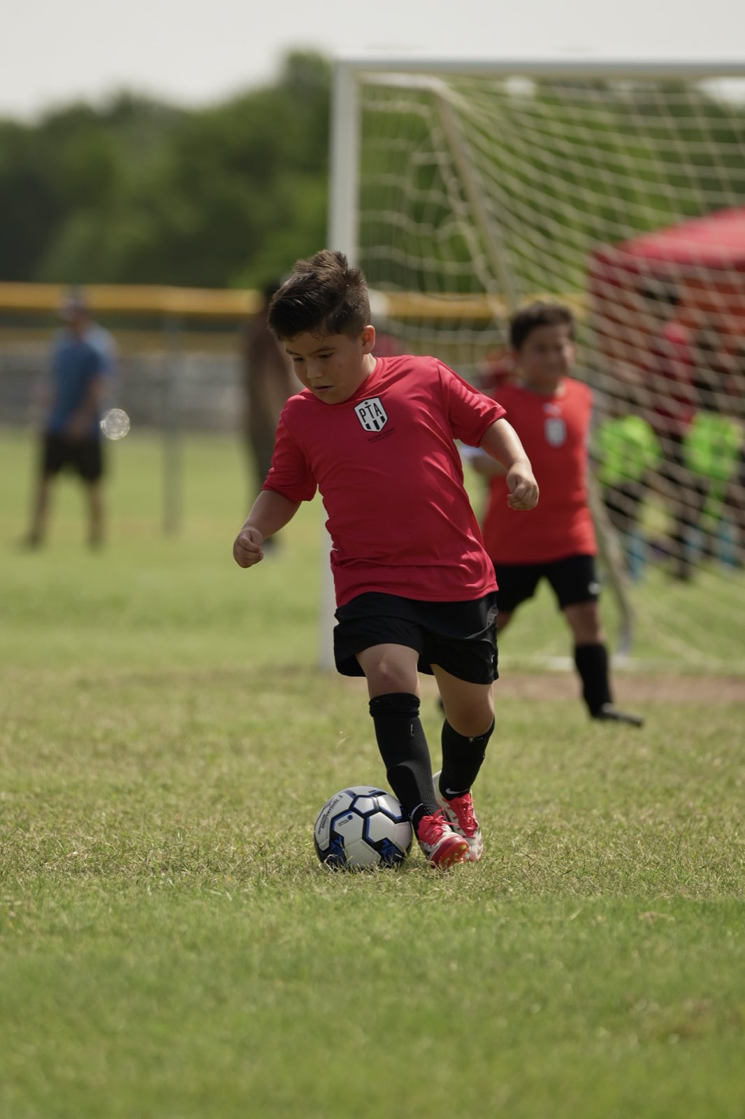 An under-10 player dribbling upfield with the goal behind him